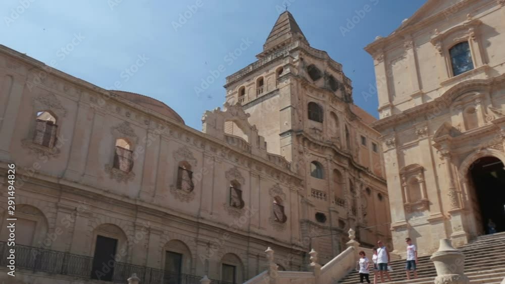 Some tourists visiting the spectacular façade of the Baroque church of S. Francesco d'Assisi and monastery of S. Salvatore in Noto, Sicily Italy. Some tourists visiting the spectacular façade of the Baroque church of S. Francesco d'Assisi and monastery of S. Salvatore in Noto, Sicily Italy.