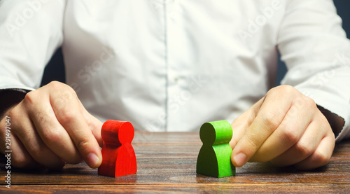 A man holds in his hands the red and green figures of people facing each other. The search for a compromise, mediation in negotiations. Weave intrigue. Conflict resolution, conflict of interest.