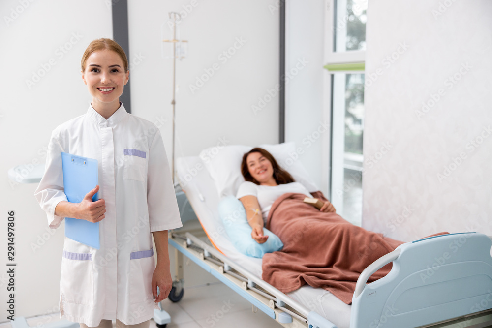 Happy female doctoe is standing near bed in clinic Happy female doctoe is standing near bed in clinic