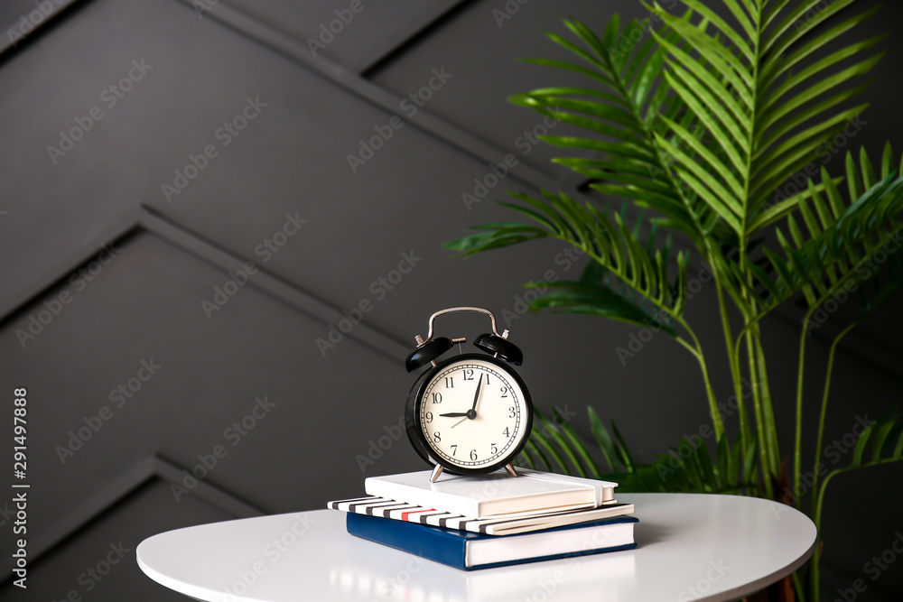 Alarm clock and notebooks on table against dark wall Alarm clock and notebooks on table against dark wall