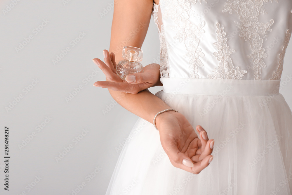 Beautiful young bride with bottle of perfume on light background Stock