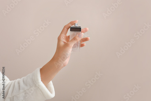 Hand of young woman with bottle of perfume on color background