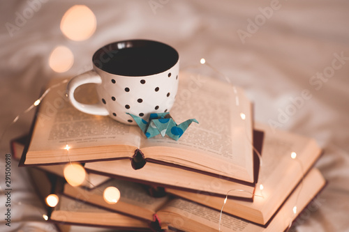 Cup of coffee with paper origami decorative crane on stack of open books closeup. School time.