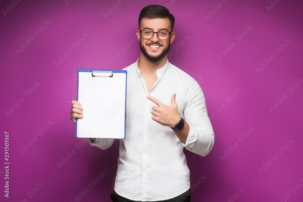 Photo of a young, business man standing against a plain violet background and smiling while he holds his leather folio. He is well-dressed in business casual and looks relaxed. Photo of a young, business man standing against a plain violet background and smiling while he holds his leather folio. He is well-dressed in business casual and looks relaxed.