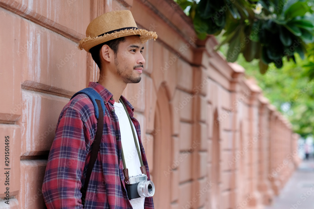 Portriat of young asian man tourist backpacker and camera standing while traveling around city in summer vacation, travel asia