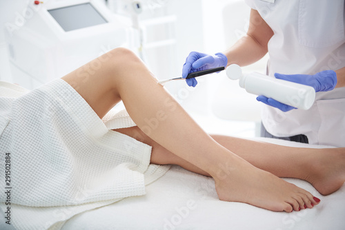 Beautician applying clear gel on lady leg before epilation