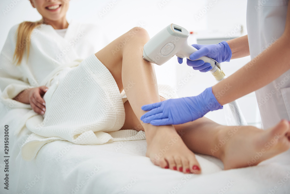 Young woman in white bathrobe receiving laser epilation in modern beauty salon Young woman in white bathrobe receiving laser epilation in modern beauty salon