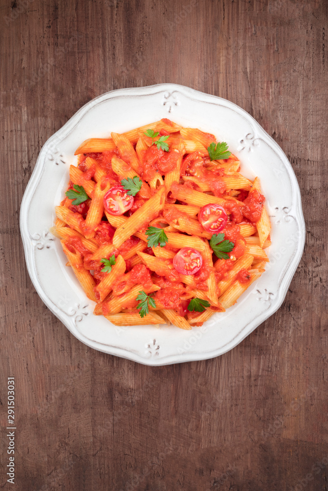 Penne pasta with tomato sauce and parsley, shot from above on a dark rustic wooden background with a place for text Penne pasta with tomato sauce and parsley, shot from above on a dark rustic wooden background with a place for text