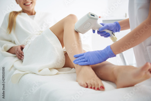 Young woman in white bathrobe receiving laser epilation in modern beauty salon