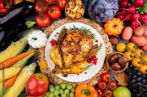 Baked chicken for Thanksgiving Day. Roasted whole chicken or turkey with autumn vegetables and fruits for thanksgiving dinner on wooden table. Healthy food for Thanksgiving Day