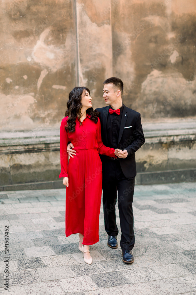 Happy and lovely Asian couple of bride and groom in the background of the old town city. Woman in red dress and man in black suit