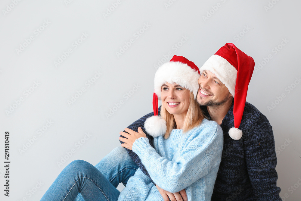 Happy couple in Santa hats on light background Happy couple in Santa hats on light background