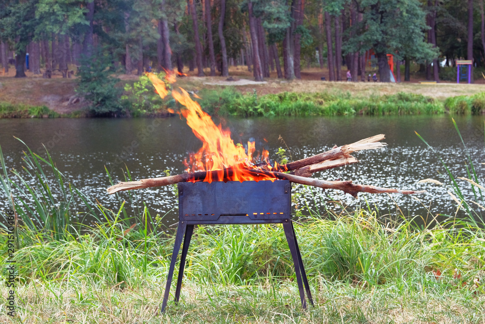 Grill. Barbecue on nature. Wood fire prepared for BBQ. Grilling season near lake or river. Picnic.