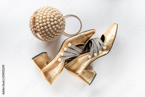 close-up of gold shoes and a gold clutch with pearls on a white background