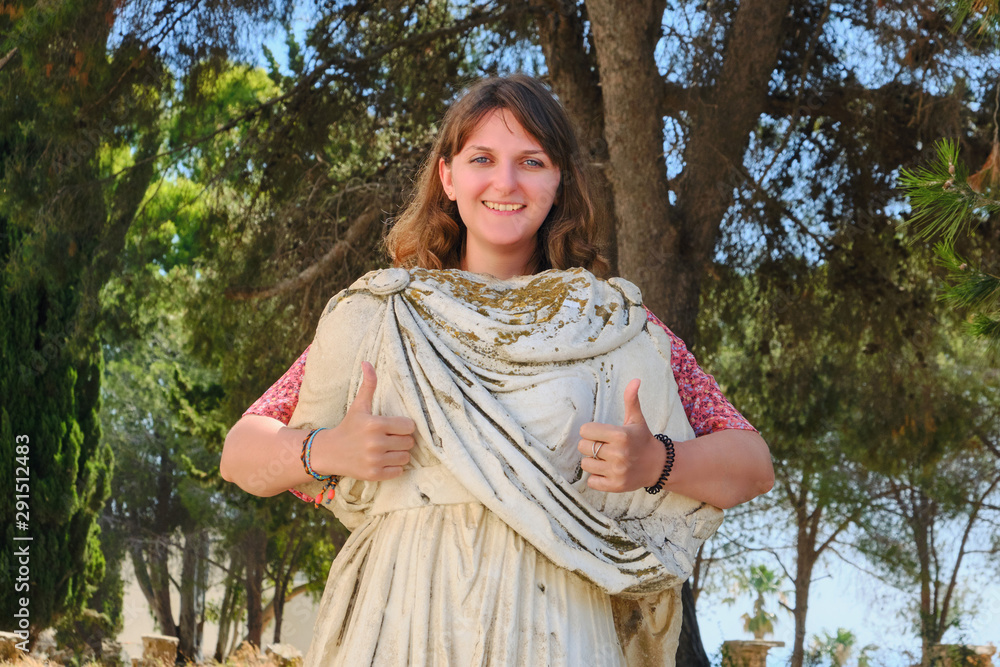 The girl shows an approving gesture with thumb up on the background of ancient statues. The girl shows an approving gesture with thumb up on the background of ancient statues.