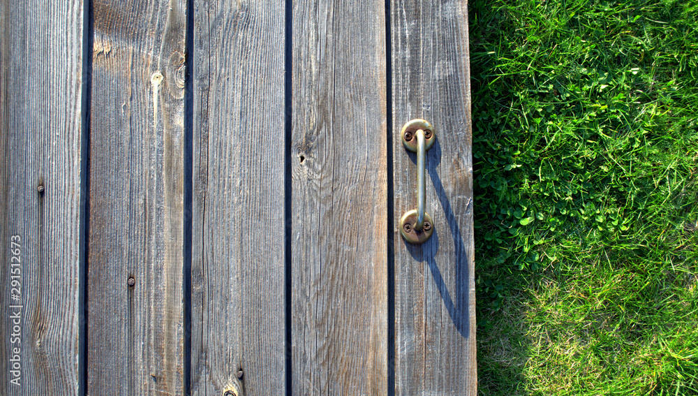 Doorknob on the background of old dark boards with soft green grass