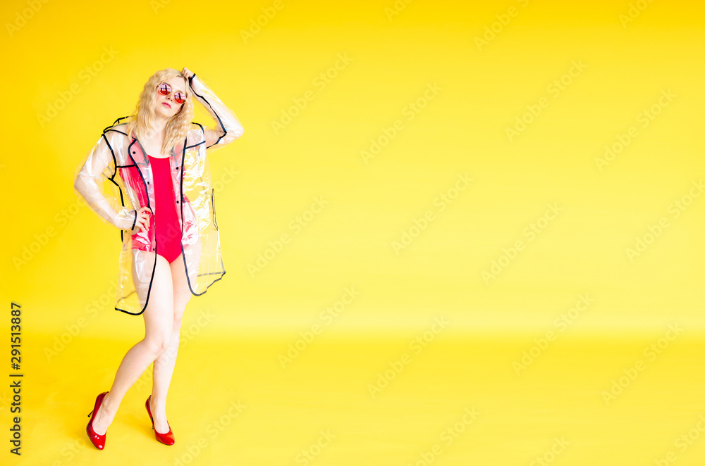 Stylish young girl in red swimmingsuit and transparent raincoat on yellow background Stylish young girl in red swimmingsuit and transparent raincoat on yellow background