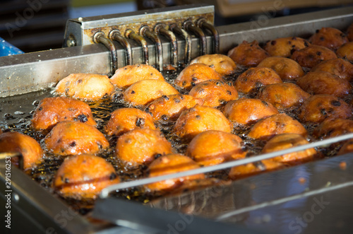 Close up of oliebollen with currants that are baking in a professional frying pan.