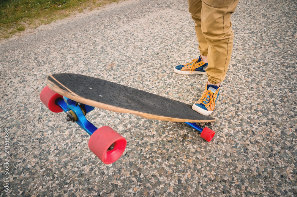 Naklejka premium Close-up of male legs in rag sneakers on a longboard on the background of asphalt at sunset. Big skateboard with man legs. Youth leisure concept