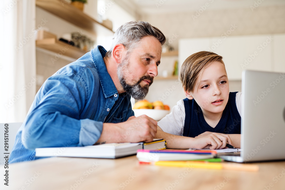 Mature father with small son sitting at table indoors, using laptop. Mature father with small son sitting at table indoors, using laptop.