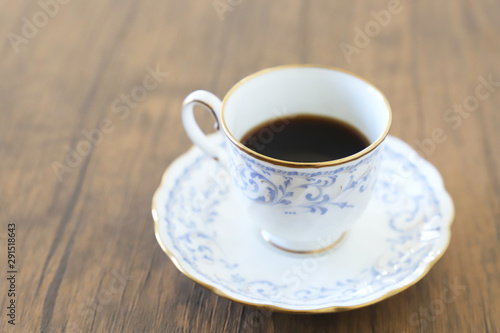 木製テーブルの上に乗った白い陶器のカップ&ソーサーにブラックコーヒー