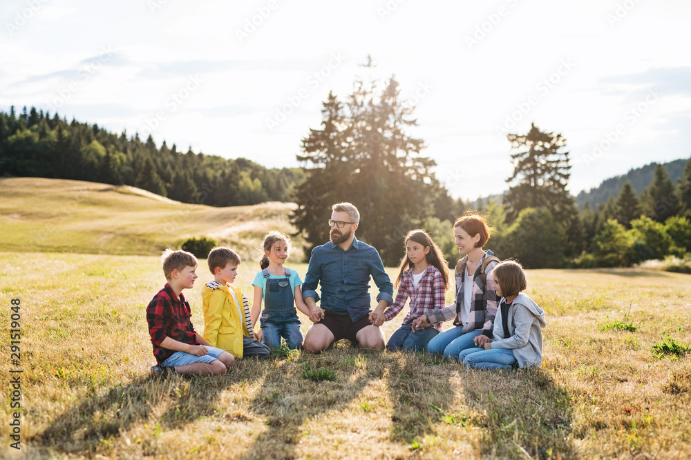 Group of school children with teacher on field trip in nature, holding hands.