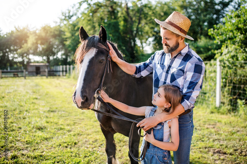 Mature father and small daughter with horse working on small family animal farm. photo