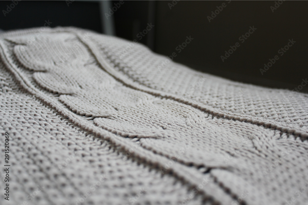 Beige knitted blanket or plaid with a braid pattern lies on the bed. Selective focus. Beige knitted blanket or plaid with a braid pattern lies on the bed. Selective focus.
