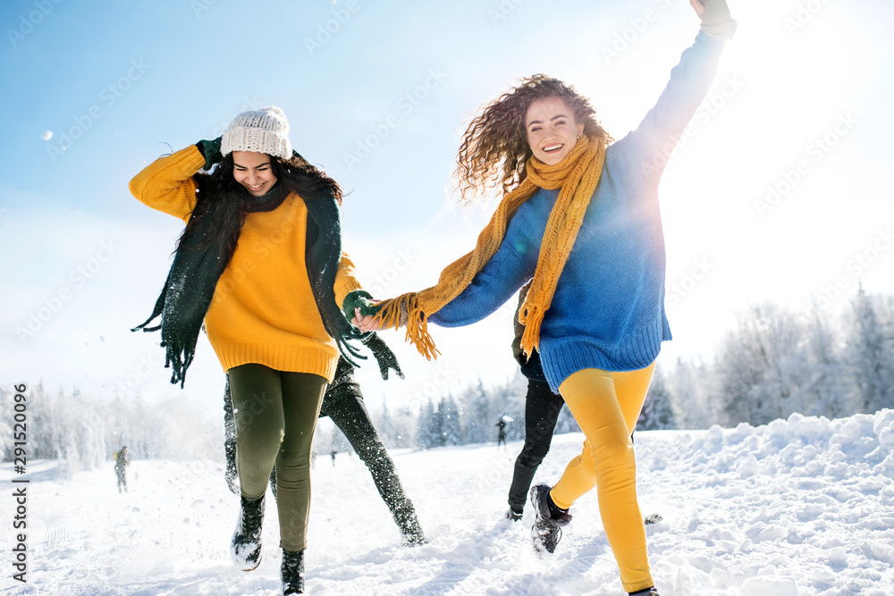 A group of young friends on a walk outdoors in snow in winter forest, running. A group of young friends on a walk outdoors in snow in winter forest, running.