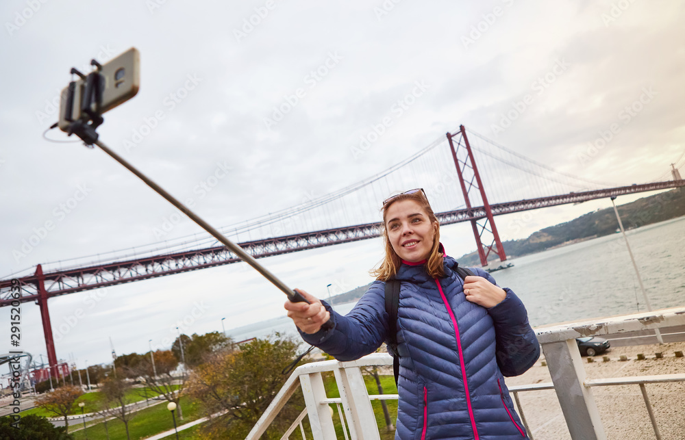 Young woman tourist take selfies on the background of famous iron 25th of April bridge in Lisbon city, Portugal Young woman tourist take selfies on the background of famous iron 25th of April bridge in Lisbon city, Portugal