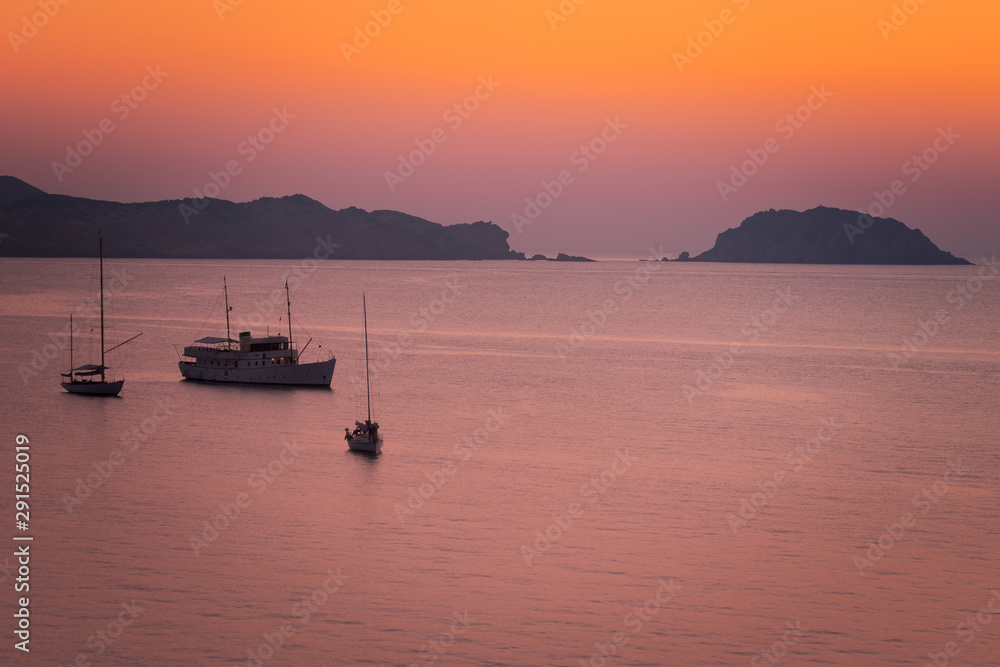 Boats seeing the sunset at August in Cavalleria beach at the north coast of Menorca, Spain.