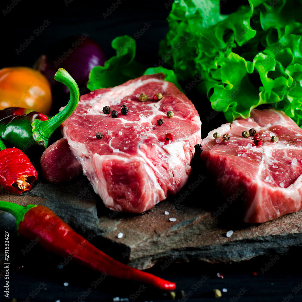 Two juicy steaks lie on a wild stone next to red and green chili peppers and a fresh green salad on a black wooden table Two juicy steaks lie on a wild stone next to red and green chili peppers and a fresh green salad on a black wooden table
