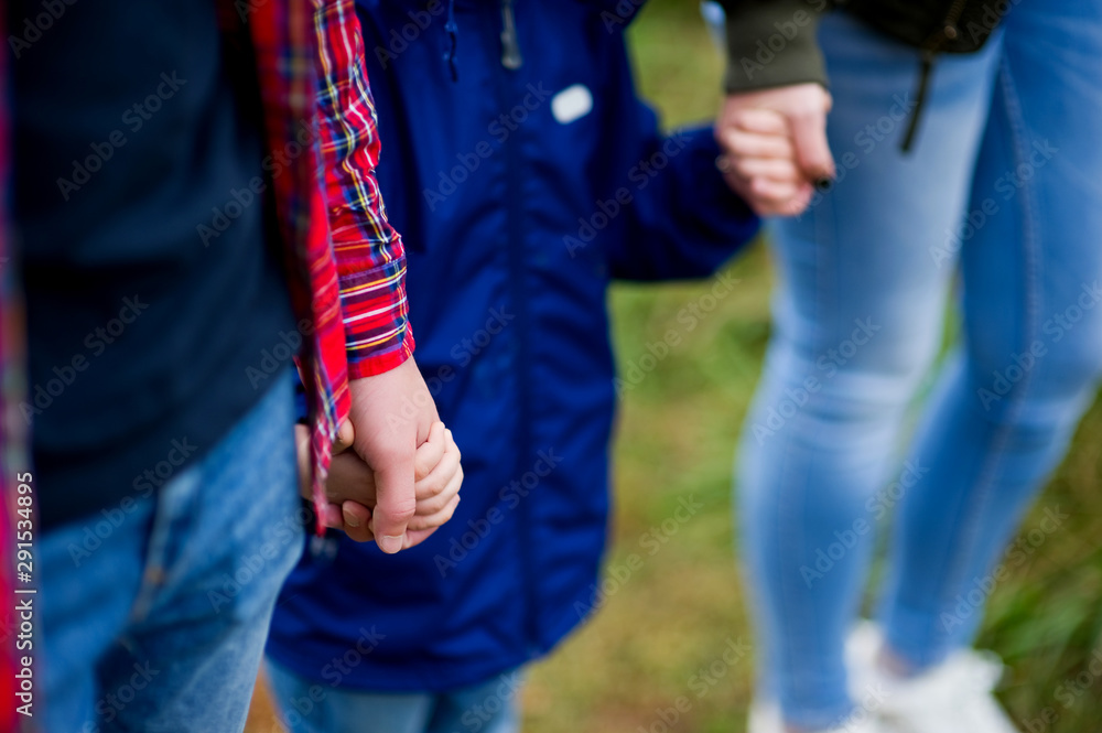 child in a blue jacket holds parents by the hands. Close-up of hands touching