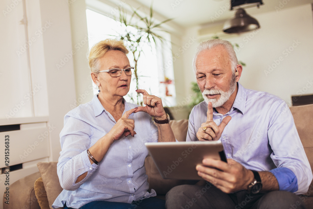 Smiling deaf senior couple talking using sign language on the digital tablet's cam Smiling deaf senior couple talking using sign language on the digital tablet's cam
