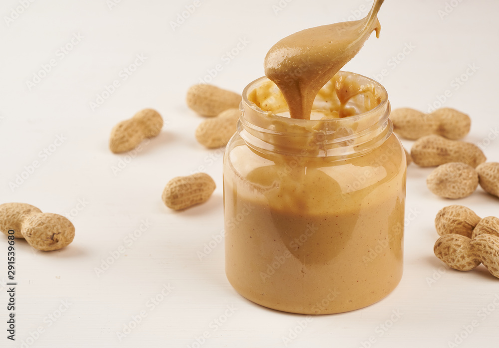 jar of peanut butter and peanuts in shell on a white table, side view, fresh ground crushed nuts, side view jar of peanut butter and peanuts in shell on a white table, side view, fresh ground crushed nuts, side view
