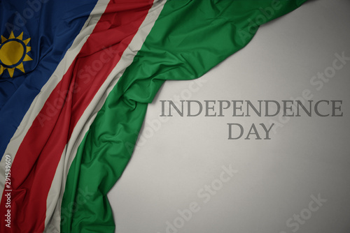 waving colorful national flag of namibia on a gray background with text independence day.