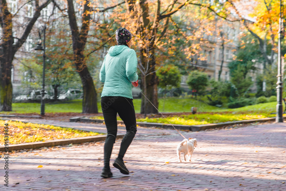 woman running with dog on leash at autumn city park woman running with dog on leash at autumn city park