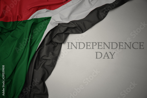 waving colorful national flag of sudan on a gray background with text independence day.