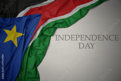 waving colorful national flag of south sudan on a gray background with text independence day.