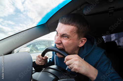 Fotografie An unbalanced, goosey man bites a car steering wheel from anger while driving in a traffic jam or after an accident