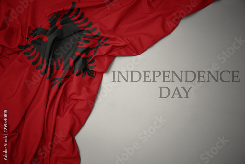 waving colorful national flag of albania on a gray background with text independence day.