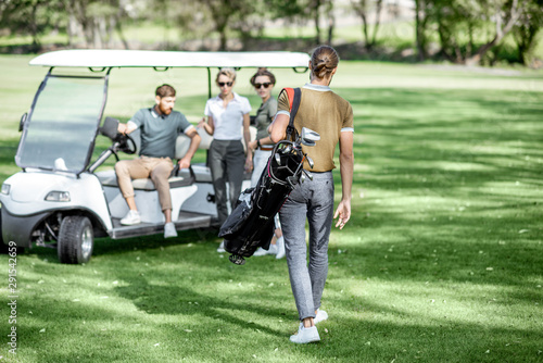 Group of a young people hanging out together near the golf car on the playing course, meeting his friend with golf bag ready ti play