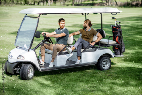 Two male best friends having fun while driving a golf car on the playing course on a sunny day