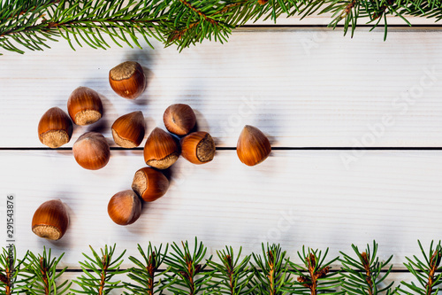 Christmas card with hazelnuts and fir branches on white wooden background