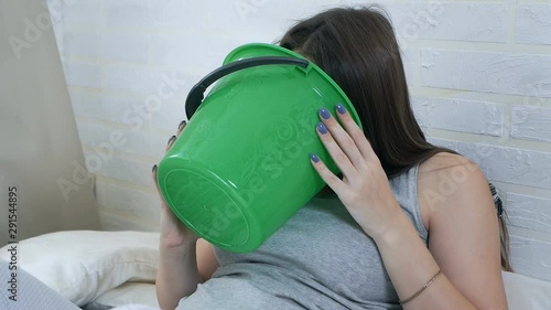 Morning sickness. Young pregnant woman lies on a couch and vomits in a bucket. Pregnancy intoxication
