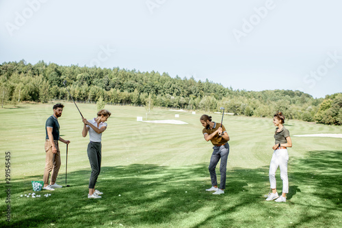 Group of a young people dressed casually playing golf on the beautiful golf course on a sunny day, man and woman swinging a putter