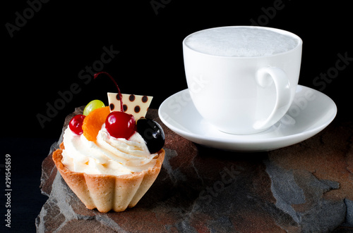 Fruit cake with cherries  grapes and plum stands on a wild stone next to a white cup of coffee with a foam