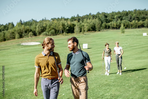 Group of friends talking and walking with putters during the golf play on the beautiful course on a sunny day