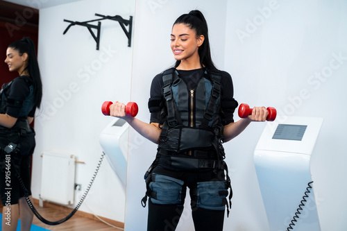 Pretty female athlete exercising with small dumb bells on ems machine  photo