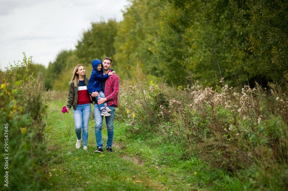 Young father, mother and son walk on a rural road, smiling